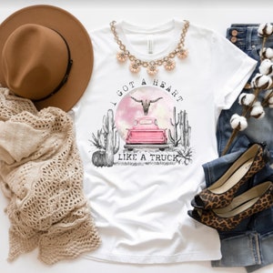 May include: White t-shirt with a pink truck, a skull with horns, and cacti. The text "I got a heart like a truck" is printed on the shirt.