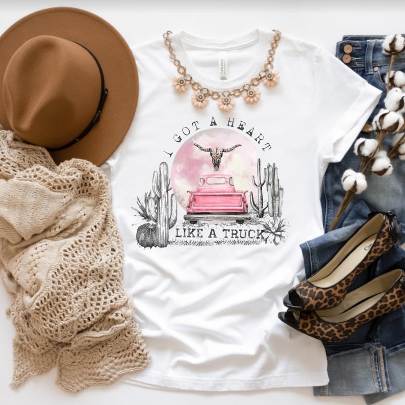 May include: White t-shirt with a pink truck, a skull with horns, and cacti. The text "I got a heart like a truck" is printed on the shirt.