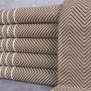 May include: A stack of brown and white chevron patterned towels. The towels are folded and have a fringe on the edge. The pattern is a repeating zigzag design. The towels are made of a soft material.