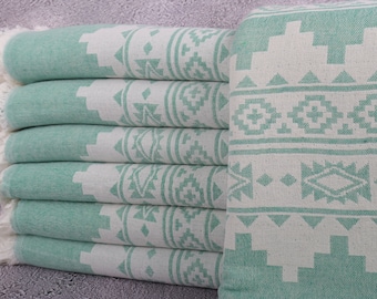 May include: A stack of six Turkish towels in a light teal and white geometric pattern. The towels have a fringed edge and are folded neatly. The design features repeating shapes and patterns.