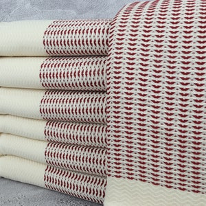 May include: Stack of six white Turkish towels with red geometric patterns. The towels have fringe on the ends.