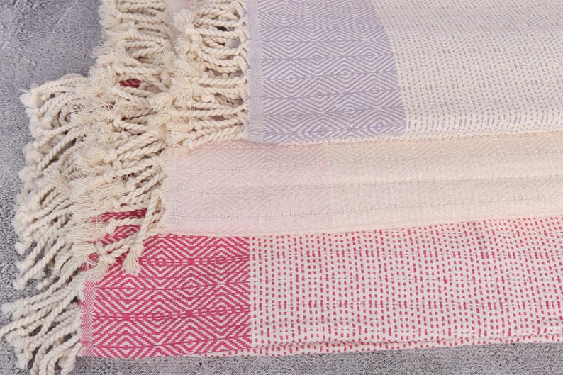 Puede incluir: Toallas de algod&oacute;n plegadas con patrones geom&eacute;tricos en blanco, rosa y lavanda. Las toallas tienen un tejido texturizado y flecos decorativos. Ideales para el ba&ntilde;o o la playa.