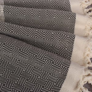 May include: A black and white patterned Turkish towel with fringe. The towel is made of cotton and has a geometric design.