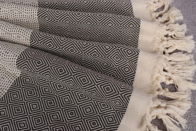 May include: A black and white patterned Turkish towel with fringe. The towel is made of cotton and has a geometric design.