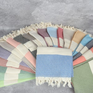 Könnte beinhalten: Eine Sammlung türkischer Handtücher in verschiedenen Farben, darunter Grün, Blau, Rosa und Orange. Die Handtücher sind gefaltet und fächerförmig angeordnet, wobei die Fransenenden sichtbar sind.
