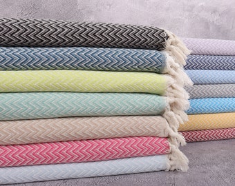 Pode incluir: Uma pilha de toalhas de algodão coloridas e tecidas com um padrão de chevron. As toalhas estão em várias cores, incluindo preto, azul, verde, rosa e amarelo. Cada toalha tem uma franja em uma extremidade.