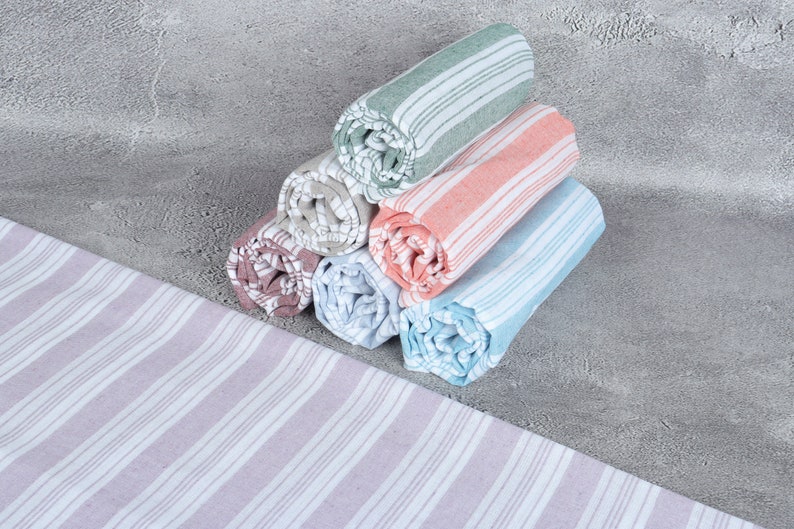 May include: A stack of six rolled towels in various colors, including green, pink, blue, and gray. The towels have a striped pattern and are arranged in a pyramid shape.