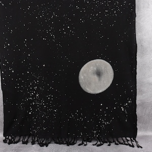 May include: Black cotton throw blanket with a white moon and stars design. The blanket has a fringe border.
