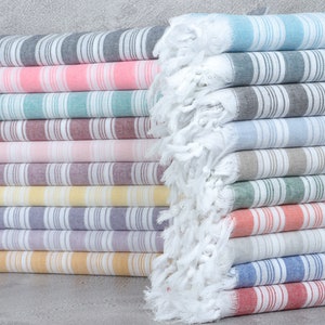 May include: A stack of striped towels in various colors, including pink, blue, gray, and yellow. The towels are made of cotton and have a fringed edge.
