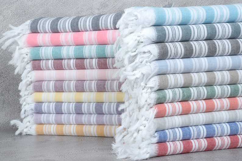 May include: A stack of striped towels in various colors, including pink, blue, gray, and yellow. The towels are made of cotton and have a fringed edge.