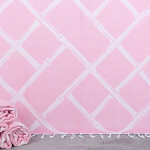 Puede incluir: Toalla de playa rosa y blanca con un patrón de estilo bambú. La toalla está doblada y enrollada, con tres toallas enrolladas adicionales visibles. La toalla tiene una franja a lo largo del borde inferior.