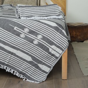 May include: A black and white striped throw blanket with a fringe border. The blanket is made of cotton and has a geometric pattern. It is draped over a bed with a wooden frame.