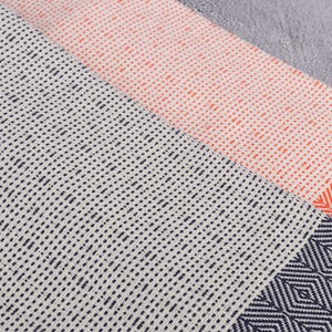 Puede incluir: Primer plano de tres textiles estampados. Uno es blanco con puntos azul marino, otro es melocot&oacute;n con puntos naranjas y el tercero es azul marino con patrones de diamantes naranjas. Los textiles son probablemente toallas o mantas.