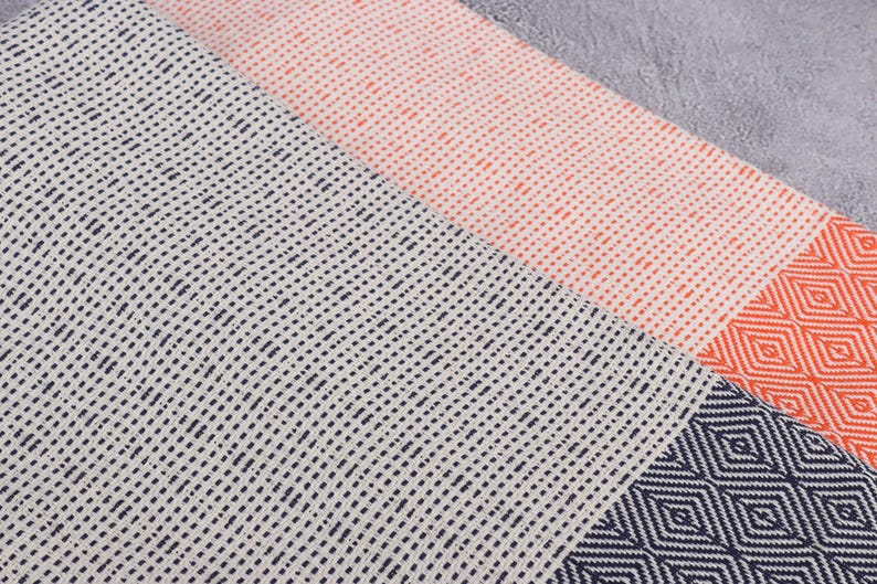 Puede incluir: Primer plano de tres textiles estampados. Uno es blanco con puntos azul marino, otro es melocot&oacute;n con puntos naranjas y el tercero es azul marino con patrones de diamantes naranjas. Los textiles son probablemente toallas o mantas.