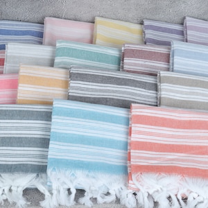 May include: A stack of striped towels in various colors, including pink, blue, yellow, and gray. The towels have a fringe border and are made of a soft, absorbent material.