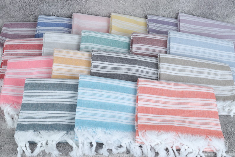 May include: A stack of striped towels in various colors, including pink, blue, yellow, and gray. The towels have a fringe border and are made of a soft, absorbent material.