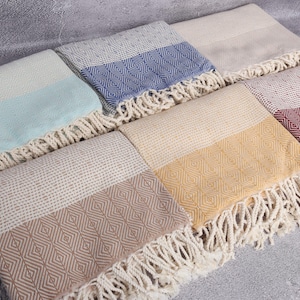 Puede incluir: Una colecci&oacute;n de toallas turcas rectangulares y coloridas con bordes con flecos. Las toallas presentan patrones geom&eacute;tricos y vienen en varios colores, incluyendo azul, amarillo y rosa. Las toallas est&aacute;n dobladas y dispuestas sobre una superficie gris.