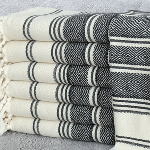 May include: A stack of white towels with black stripes and diamond patterns. The towels have fringe on the edges.