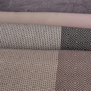 May include: A stack of four woven towels with different patterns. The top towel is pink with a diamond pattern, the second towel is white with a black diamond pattern, the third towel is white with a black wavy line pattern, and the bottom towel is beige with a brown diamond pattern.