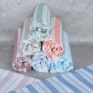 May include: A stack of rolled striped towels in various colors, including pink, blue, green, and beige. The towels are arranged in a pyramid shape on a gray textured surface.