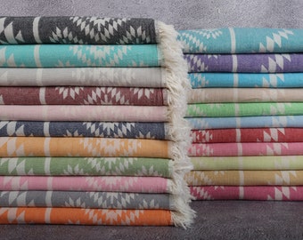May include: A stack of colorful Turkish towels with geometric patterns. The towels are in various colors, including teal, gray, pink, and orange. Each towel has a white geometric design and a fringed edge.