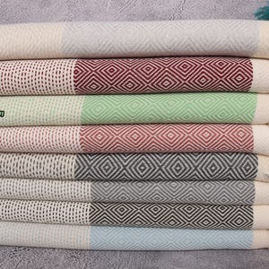 May include: A stack of eight Turkish towels in various colours, including light grey, burgundy, apple green, brick, anthracite, dark grey, dark green, and baby blue. Each towel has a diamond pattern and a fringe.