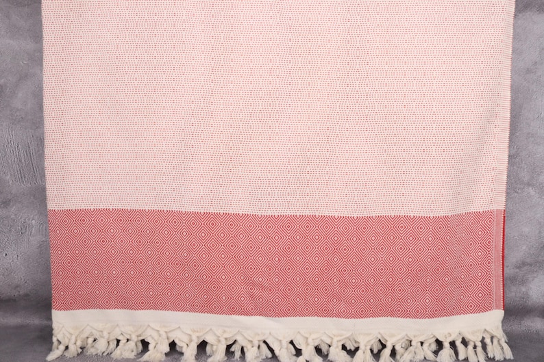 May include: A white and red Turkish towel with a diamond pattern. The towel has a fringe border.