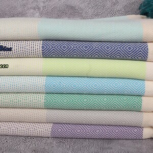 May include: A stack of seven Turkish towels in various colours, including mint, turquoise, pistachio green, light grey, and lilac. Each towel has a white border and a diamond pattern.