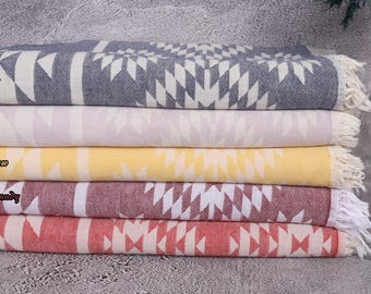 May include: Five patterned Turkish towels stacked on top of each other. The towels are in the colors navy, lilac, yellow, burgundy, and red. The towels have a white fringe.