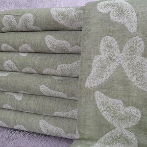 May include: A stack of six folded green towels with a white butterfly pattern. The towels have a fringed edge and are made of a soft, textured fabric. The butterfly design is repeated across the towels.
