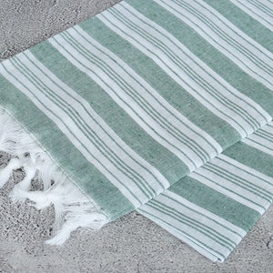 May include: A green and white striped Turkish towel with white fringe. The towel is folded in half and the fringe is visible on one side.