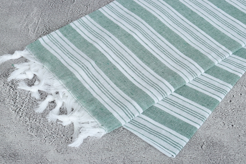 May include: A green and white striped Turkish towel with white fringe. The towel is folded in half and the fringe is visible on one side.