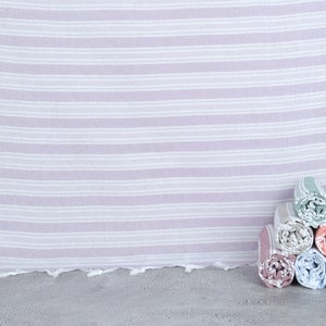 May include: A stack of six rolled towels in various colors, including pink, blue, green, and peach, with a white and light purple striped towel in the background.