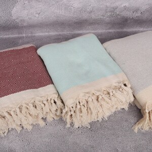 May include: Three Turkish towels with fringe. One towel is red with a diamond pattern, one is light blue, and one is grey.