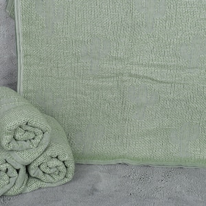 May include: Three rolled up green towels stacked on top of each other. A larger green towel is lying flat behind the rolled towels.