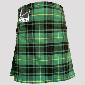 Op de afbeelding: Een groene, zwarte en gele tartan kilt met een franje aan de onderkant. De kilt heeft een label met de tekst "Traditionele Kilt".
