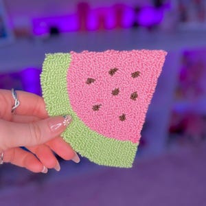 May include: A pink and green watermelon-shaped needlepoint piece with brown seeds.