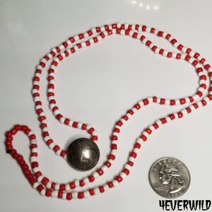 May include: A red and white beaded necklace with a silver coin pendant. The necklace is about the size of a US quarter.