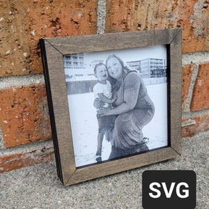 Könnte beinhalten: Ein Schwarzweißfoto einer Frau und eines Kindes am Strand, gerahmt in einem dunklen Holzrahmen.