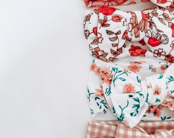 May include: Four floral print headbands with bows. The headbands are in a variety of floral patterns with pink and white backgrounds. The bows are tied in a knot and are made of the same fabric as the headband.