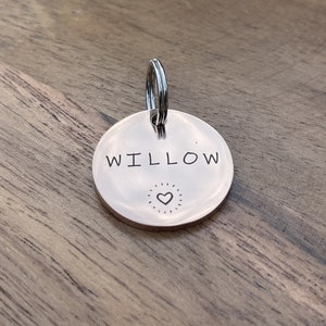Op de afbeelding: Ronde zilveren dierenpenning met de naam "WILLOW" erop gegraveerd en een klein hartje onder de naam.