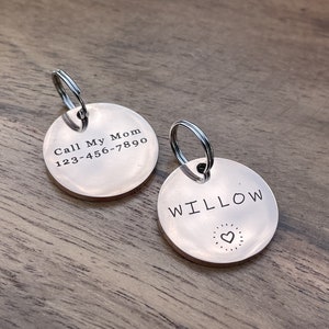 Op de afbeelding: Twee zilveren hondenpenningen met sleutelringen. Een penning zegt "Call My Mom 123-456-7890". De andere penning zegt "WILLOW" met een klein hartje.
