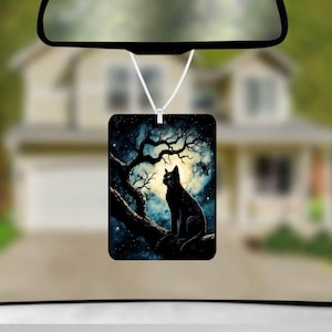 May include: A rectangular car air freshener hanging from a rearview mirror, featuring a printed illustration of a black cat sitting on a tree branch against a backdrop of a bright full moon, a dark blue night sky, and scattered stars.