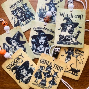 May include: Set of ten vintage-style Halloween-themed car air fresheners. Each card features a witch with a different saying, including "Squad Ghoul", "Spooky Early", "I'm Made Out of Glitter", "Witchcraft", "Girls Trip", and "Howdy Witches".
