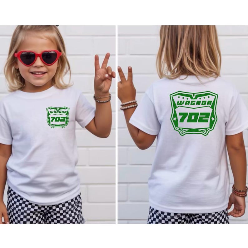 May include: A white short-sleeved t-shirt featuring a green graphic on the front left chest and a larger matching green graphic on the back. The graphic displays the text WAGNOR above the number 702 inside a shield-shaped border with stars.