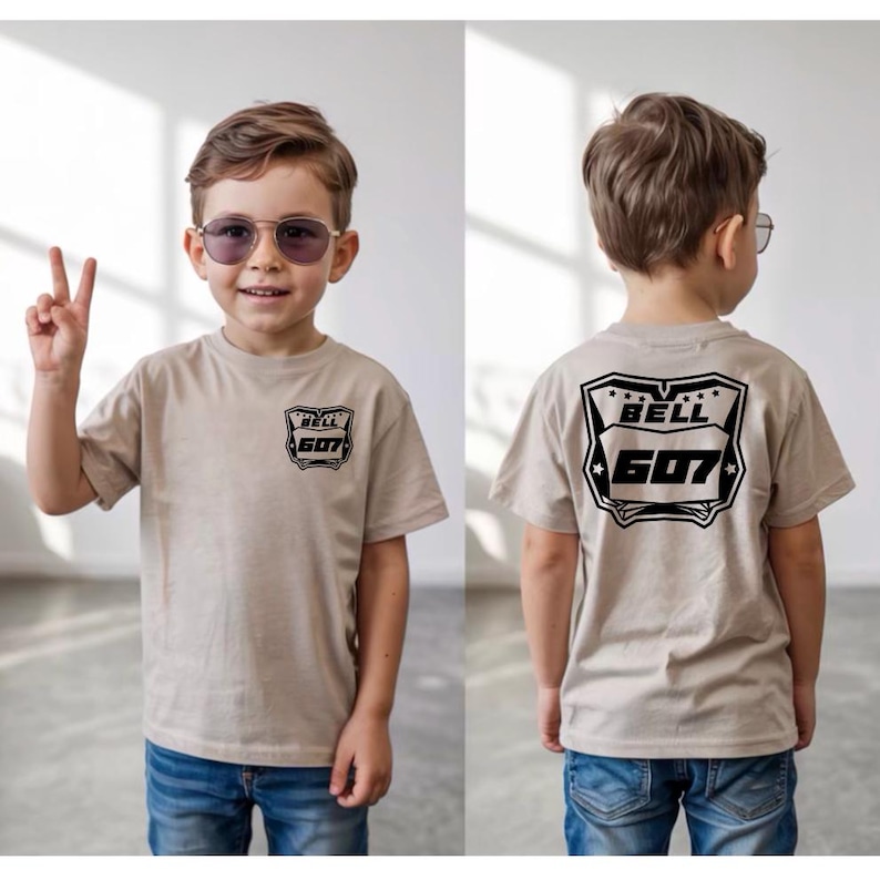 May include: A beige short-sleeve t-shirt featuring a black graphic on the front left chest and a larger matching black graphic on the back. The graphic displays the text BELL 607 inside a shield-like emblem with small stars at the top.