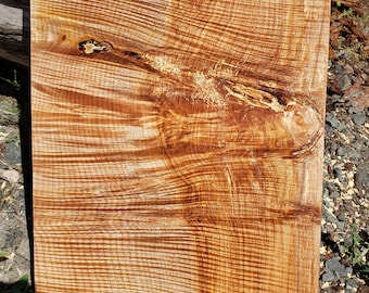 May include: A close-up of a piece of wood with a unique grain pattern. The wood is a light brown color with darker brown streaks running through it. The wood has a natural, rustic look.