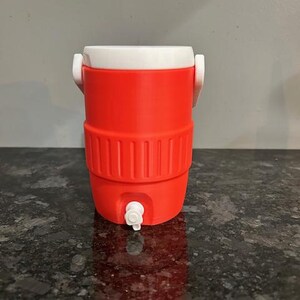 May include: A red and white water cooler with a spigot. The cooler has a white lid and handle, and a ribbed design around the middle. It is designed to hold liquids and keep them cool. The cooler is made of plastic.