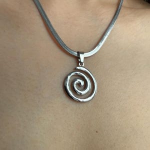 Close-up detail of the 3cm by 2cm swirl pendant, showcasing the durable surgical-grade stainless steel texture and liquid-like movement of the chain.