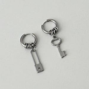 Op de afbeelding: Zilverkleurige oorringen met unieke bedels. Eén oorring heeft een hangslotbedel, de andere een sleutel. De oorbellen zijn eenvoudig en stijlvol ontworpen, geschikt voor dagelijks gebruik. Gemaakt van zilverkleurig metaal.